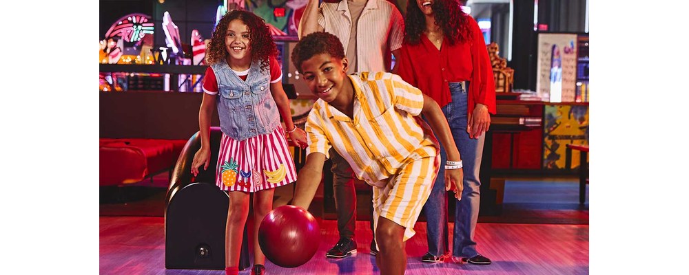 Kids bowling at a Bowlero center with family behind them