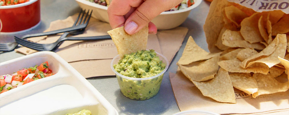 A tortilla chip dipped into Chipotle guacamole beside a pile of tortilla chips