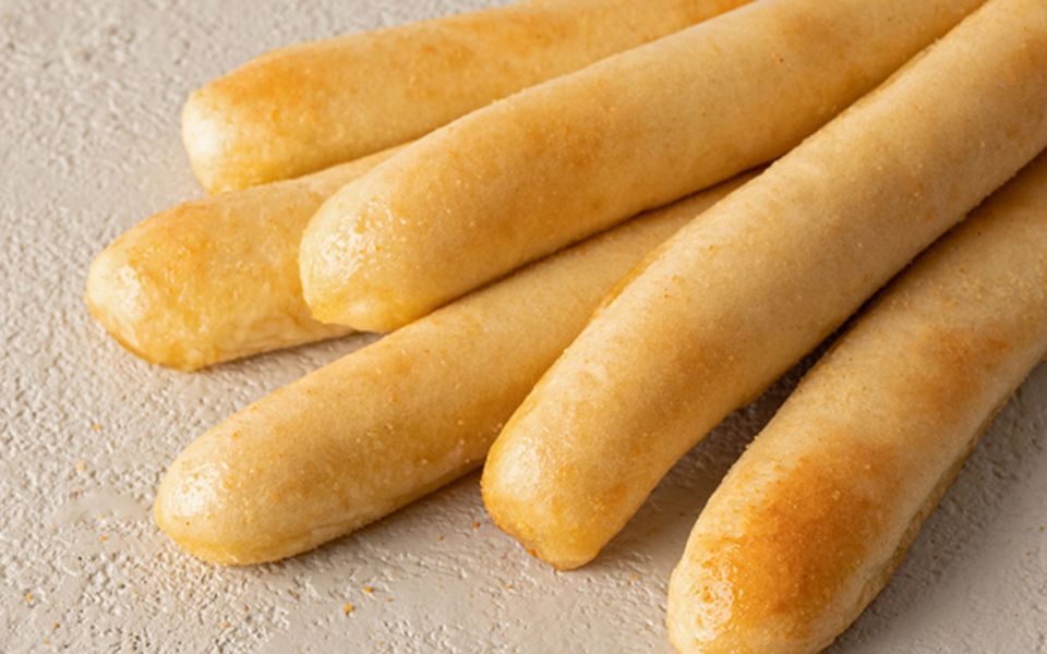Six golden breadsticks on a lightly floured surface