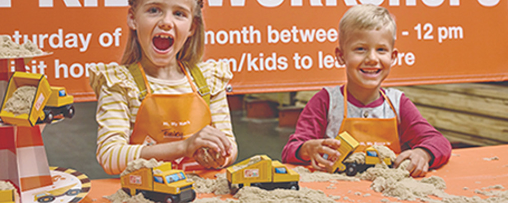Two children displaying yellow wooden dump trucks at a Home Depot Kids Workshop.