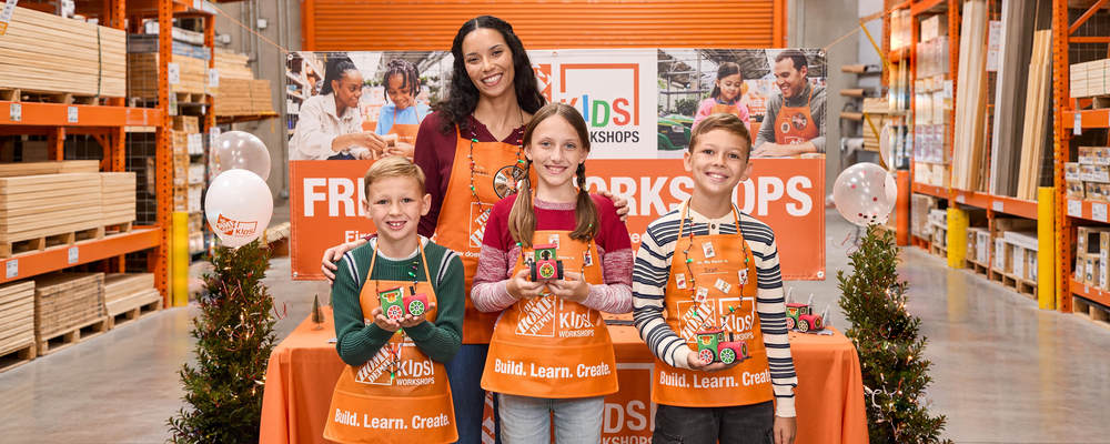 Home Depot workshop associate and children displaying holiday train projects.