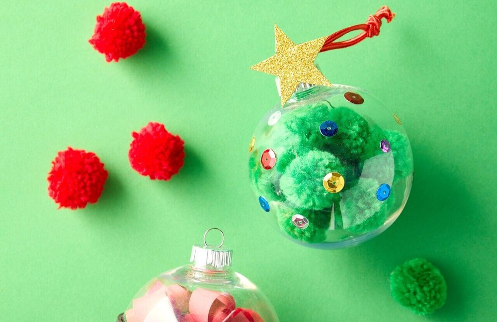Two clear holiday ornaments filled with green pom-poms on a green background