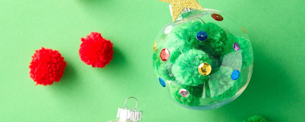 Clear ornament filled with green pom-poms and sequins, with red pom-poms on green