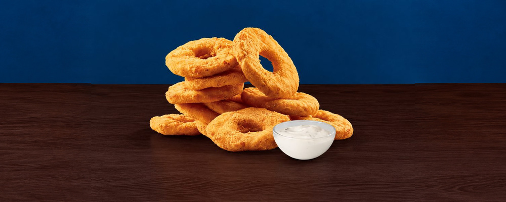 A stack of golden breaded chicken rings beside a white bowl of dip